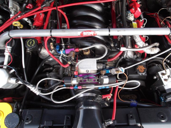 A close up of a motorcycle on display - Pistonheads - The image is a close-up photograph of the engine bay of a vehicle. There are many colorful engine belts, wiring, and possibly fuel lines visible. The components are tangled and organized to manage complex electrical and mechanical systems. A black battery with red and yellow wires around it is also evident. The photograph captures the under-hood view of automotive repair work, showcasing the complexity and intricacy of the engine's structure.