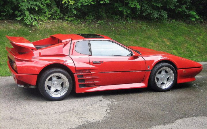 RE: Extraordinary Ferrari 288 GTO Evoluzione for sale - Page 1 - General Gassing - PistonHeads UK - The image shows a classic red sports car parked on the side of a road. It's an old-style coupe, possibly from the 1980s or 1990s, with large flared wheel arches and a wide stance. The vehicle has a distinctive design, featuring prominent front and rear wings, which are indicative of classic race cars. The car also appears to have a significant amount of custom modifications or aftermarket parts, enhancing its sporty appearance.