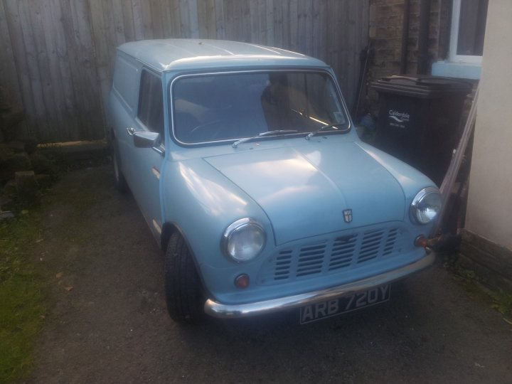 Pictures Of Your Minis! - Page 1 - Readers' Cars - PistonHeads - The image shows a light blue vintage car parked on a driveway. The car is viewed from a front right perspective. It has large round headlights and a prominent grille. The car is positioned in front of a wooden privacy fence and there is a black trash bin nearby. The setting suggests a residential area.