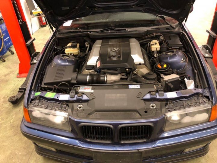 E36 V8 Fun - Page 1 - BMW General - PistonHeads - The image shows a vehicle with its hood open, revealing the engine and various mechanical components. The car appears to be a BMW model, identifiable by the badge on the trunk lid. It is parked inside a building, under what seems to be fluorescent lighting. The car's hood is propped up, suggesting it may be under repair or maintenance. There are various tools and parts scattered around the vehicle, indicating that work has been or is being done on it.