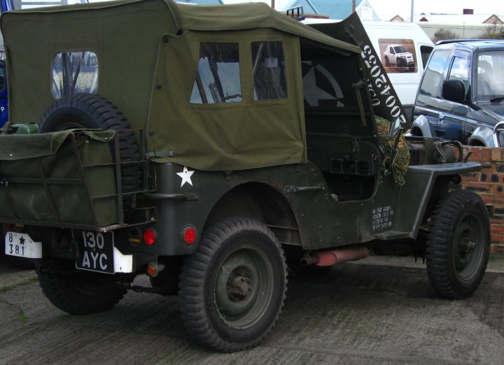 Glazier/glass cutter in NE open tomorrow (Sat 8th) - Page 1 - North East - PistonHeads - The image displays a vintage military jeep parked on a concrete surface. The vehicle is painted in army green and has covered cargo areas at the back. A large number, which is "S 593700", is printed on the front side door. The wheels and tires appear to be sturdy and suitable for off-road use. In the background, there's an old-fashioned car and a brick wall. A single star is visible on one of the cargo areas.