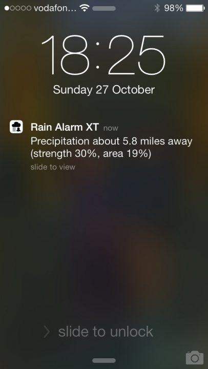 A close up of a person holding a pair of scissors - Pistonheads - The image shows a screenshot of a smartphone displaying the phone's status bar. It's 18 hours and 25 minutes when the photo was taken, as indicated by the digital clock. The date is Sunday, October 27th. The battery status shows a reading of 98% at the top right of the device. The main notification on the screen is about a "Rain Alarm XT." The announcement is that there will be precipitation about 5.8 miles away, with a 30% likelihood, but the notification does not provide precise details about the severity or type of precipitation. The lock screen button is visible at the bottom, suggesting this is the status bar screenlocked on a phone brand.
