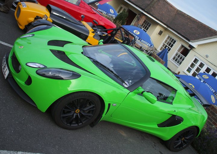 Pub Pistonheads July - The image showcases a lineup of four unique sports cars. The cars display a spectrum of colors ranging from vibrant green, to striking red, to a neutral yellow. They are parked in an orderly fashion, possibly in a hotel parking lot as suggested by the structure in the background. The setting appears to be a sunny day, and the cars are unused, indicating they may be on display or temporarily parked.