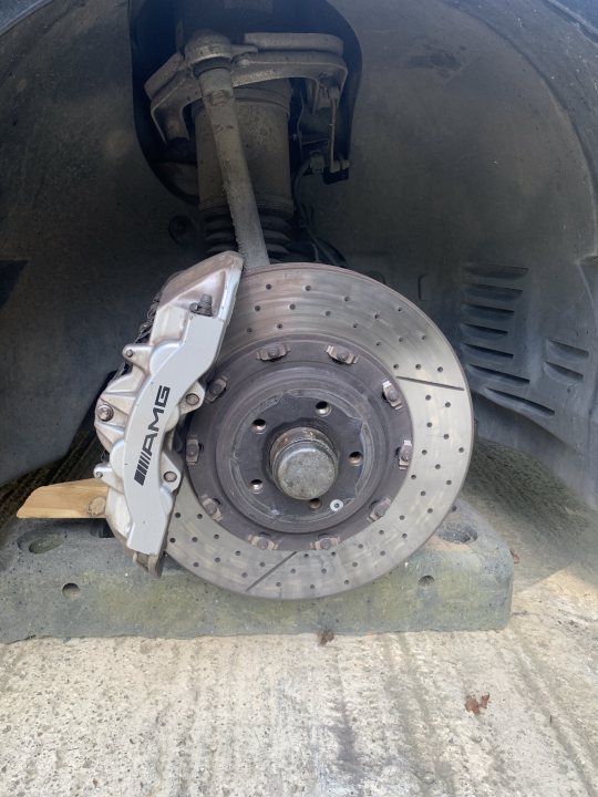 Drilled disk cracks - when to change - Page 2 - Suspension, Brakes & Tyres - PistonHeads UK - The image shows a car with its front wheel removed, revealing the brake rotor and various components of the braking system. The brake rotor has multiple caliper pistons attached to it, suggesting an enhanced or aftermarket braking setup. The vehicle appears to be parked in an outdoor setting during daylight hours. There are no visible texts or brands on the car or its components. The style of the image is a straightforward, real-world photograph with no apparent filters or artistic manipulations.