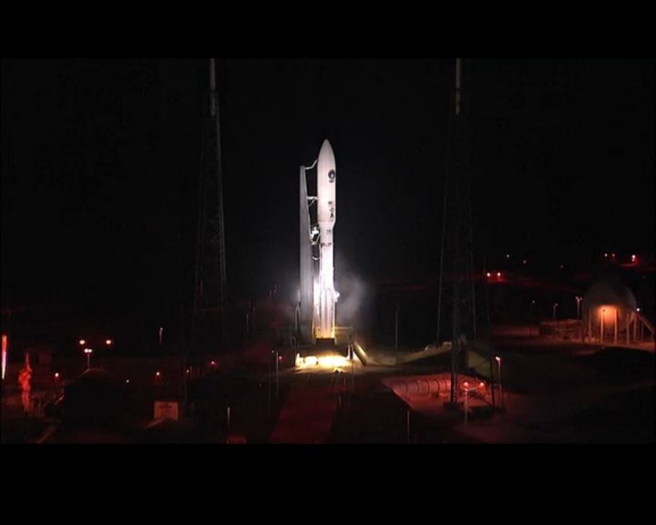 Atlas V launch tonight - Page 1 - Science! - PistonHeads - The image captures a magnificent night scene at a space center. The central focus is a large, white space shuttle that is prominently displayed. The shuttle is modern, with a sleek design. Situated on a launchpad, the shuttle appears to be ready for an upcoming launch. The launchpad is illuminated by various lights, with warm yellow and blue hues surrounding the base of the shuttle. The black sky overhead contrasts with the artificial lights, making the shuttle the unquestionable star of the image. The overall image depicts the anticipation and preparation surrounding space exploration.