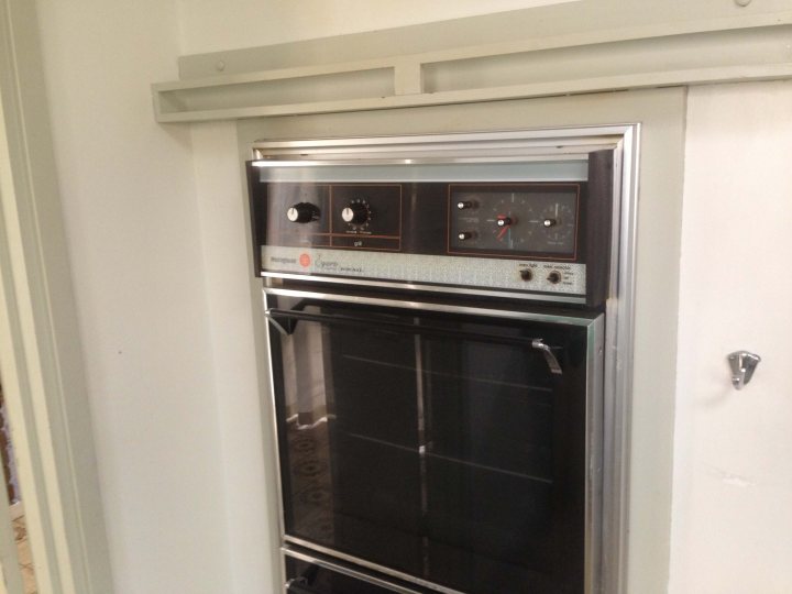 A stove top oven sitting inside of a kitchen - Pistonheads - The image shows an interior view of an electric oven installed in a wall with a white door. The oven's control panel is on the right side. It appears to have multiple knobs and possibly a digital display or dials for various cooking functions. The oven door has a visible glass window, and the overall color scheme suggests it might be a stainless steel model. The oven is outlined by a metallic border, and there's a mounting plate or frame around it, likely for ensuring that the oven is securely fixed to the wall.