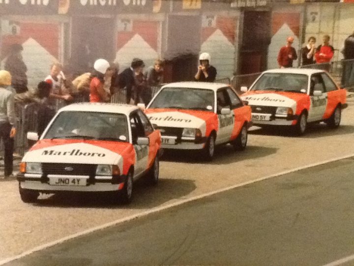 A group of police officers on a city street - Pistonheads - This image captures a scene from a Marlboro race at a dirt track. Three identical cars, painted in the company's iconic livery, are racing around the bend. Spectators are scattered around the venue, with some of them standing on the pavement, while others are inside the white tent on the side of the track. The cars themselves are from the Falcon model range, indicating that this might be an Australian racing event. The atmosphere seems charged with anticipation, typical of a thrilling race day.