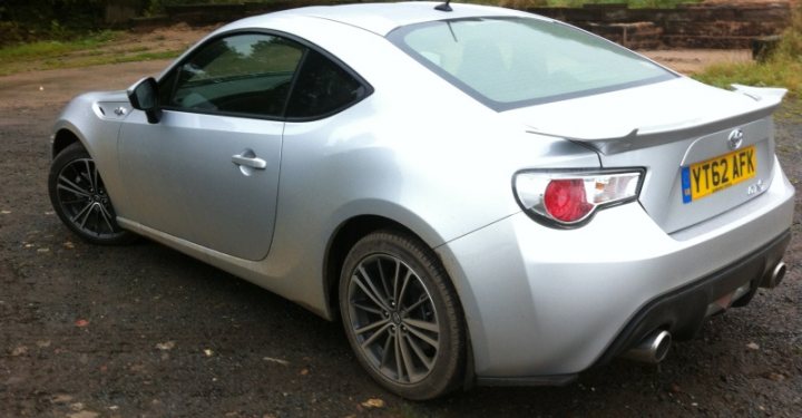 A car parked in a parking lot next to a car - Pistonheads - The image depicts a silver two-door car parked on what appears to be an uneven surface or pavement. The car is a compact model, as indicated by its body shape and size. The paint on the car shows a slight sheen, suggesting it may be a newer model or well-maintained. The license plate of the car reads "YT62 KV" and is located at the rear. The car has a single visible side mirror. The surrounding area includes grass and some hints of an outdoor environment, providing context that the car is parked in an area with greenery.