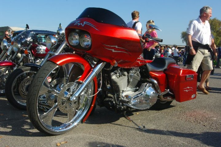 breakfast club sunday october 2 - Page 1 - Goodwood Events - PistonHeads - In the heart of a parking lot, where several motorcycles are parked in a row, a competitive racing motorcycle stands out. This red motorcycle, adorned with a racing angel logo, commands attention with its prominent shine. A person is standing next to it, perhaps admiring the craftsmanship or preparing for a ride. In other parts of the parking lot, more individuals can be seen, but they are primarily in the background, adding depth to the scene.