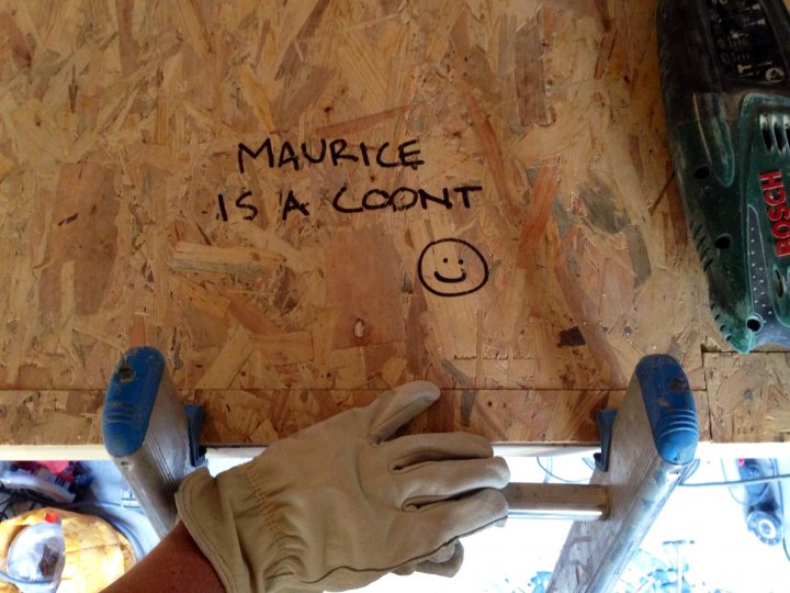 Chamonix studio renovation - build thread - Page 4 - Homes, Gardens and DIY - PistonHeads - The image shows a piece of plywood with some writing on it. The writing is in black marker and says "Maurice is a coont". Below the writing is a smiley face drawn in blue marker, accompanied by a winking emoticon and a heart symbol. Underneath this, there is a verification logo for Adidas. A hand is visible in the image, touching the plywood, likely referencing the author of the text. The background reveals an indoor setting, possibly a workshop or a house being built, indicated by power tools and a person working.