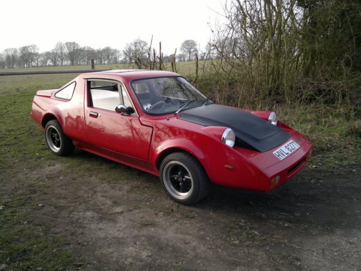 Is there a Market for an Inexpensive Hillclimb Car ? - Page 1 - UK Club Motorsport - PistonHeads - The image showcases a red sports car parked on a dirt field, with a license plate reading "J2 871". The car is designed with distinctive features, including a large rear window and a prominent spoiler. The vehicle's color and style suggest a sportier or racing-oriented bias, and its rugged setting contrasts with what would be a more common urban or roadside location for such a vehicle. The background reveals a greenery-dotted field, indicating a countryside or rural setting.