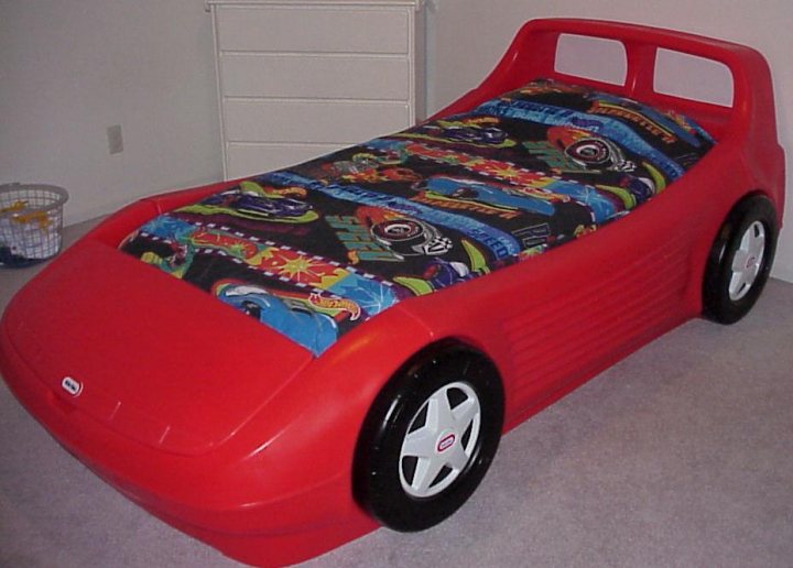 RE: Ferrari F50: Time For Tea? - Page 3 - General Gassing - PistonHeads - The image features a child's car bed. The bed is shaped like a vehicle with a vibrant red and black color scheme. On top of the bed lies a blanket with a cartoonish design, adding to the playful theme of the bed. The bed and dragon are in a room, with a wicker basket also visible in the background. The bed covers the entire image frame, indicating its substantial size.