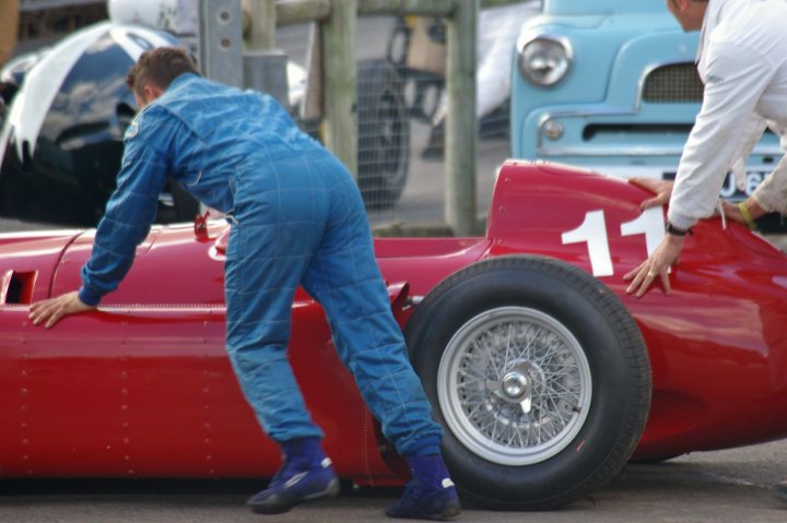 2012 Goodwood Revival Meeting Photo Gallery - Page 1 - Goodwood Events - PistonHeads - In the image, two men are inspecting a classic red Alfa Romeo car with the iconic number "11" painted on its side. The car is sleek, with a shiny red body and black tires, standing out against the backdrop of a garage or track. The man on the left, dressed in a blue jumpsuit, is bent over, inspecting the car closely. The man on the right, wearing a white jumpsuit, is also closely examining the car, holding onto the hood as if showing it off. The scene suggests a setting of racing or vintage vehicle maintenance.