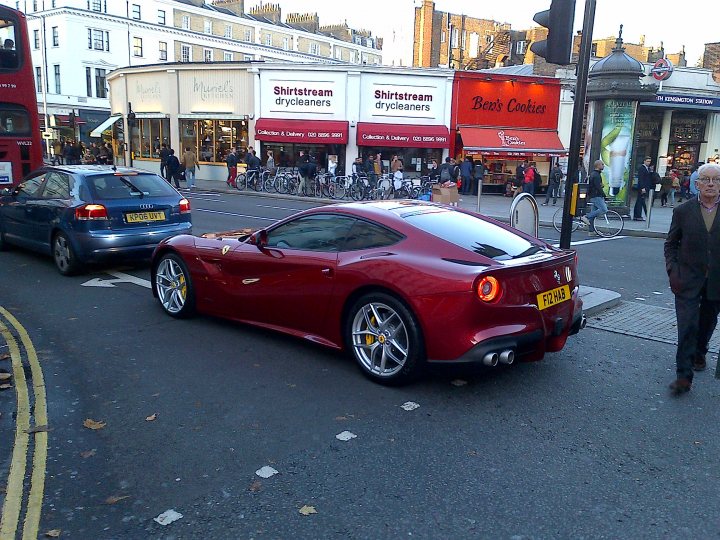 Supercars spotted, some rarities (vol 6) - Page 131 - General Gassing - PistonHeads - In the heart of a bustling city, a vibrant red sports car takes the spotlight as it cruises down a busy street. The car's sleek design, vibrant color, and shiny finish make it stand out among the other vehicles. Its yellow license plate adds a touch of brightness, matching the cheerful demeanor of its surroundings.

The street is alive with people going about their day. Cars are positioned in both directions, reflecting the constant motion of city life. Bicycles are scattered throughout the scene, some ridden by energetic individuals, others perhaps locked to a nearby pole, resting after a long ride.

Adding to the charm of the scene are trees lining the sidewalk, providing a touch of nature amidst the urban landscape. In the distance, a red double-decker bus can be seen, hinting at the city's well-connected public transportation system. The scene encapsulates a perfect day in a lively city where life moves at a fast pace.