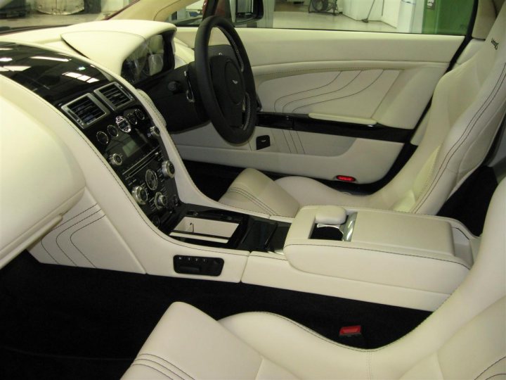 Six Weeks of V8VR S Ownership - Page 1 - Aston Martin - PistonHeads - The image shows the interior of a luxury vehicle with a white cabin and black leather seating. The dashboard features a center console with a digital display screen and control knobs, indicative of advanced features and navigation systems.