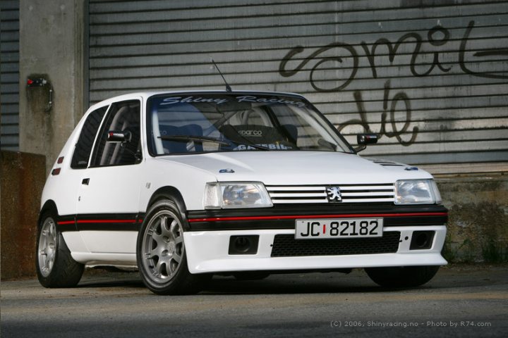 Market Alloys Pistonheads - The image depicts a white hatchback car parked next to a concrete wall. The car features striking black and red stripes on the side, a detail that adds a sporty and unique touch to its appearance. The license plate on the car is clearly visible, with the registration reading 'JC 82182'. The wall behind the car has some spray paint on it, although the text is not entirely legible. The car's design, with its dynamic lines and sporty trim, suggests it could be a high-performance vehicle.