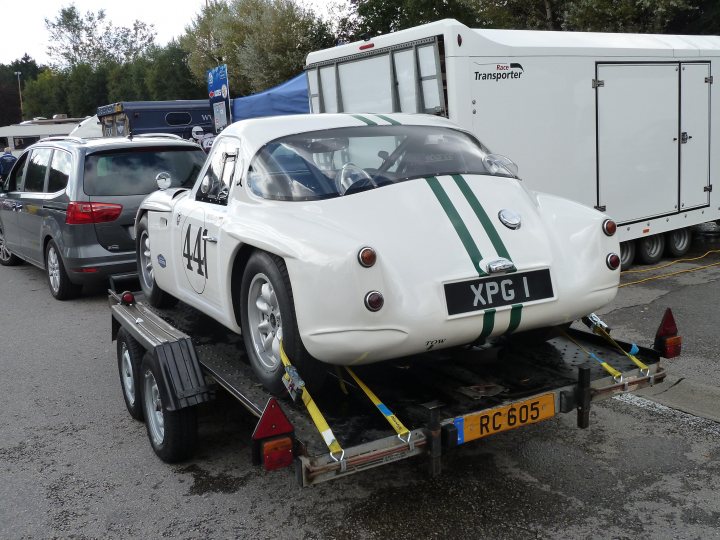 Spa 6 hours, 2015 - Page 1 - Classics - PistonHeads - The image features a vintage, white racing car with bold green stripes and the number "44" prominently displayed. It's being towed by a flatbed trailer, as indicated by the yellow straps and rims attached to the car. The car is being hauled on a road that is covered with wet leaves. On the side of the road, there is a white trailer with a sign that reads "TRANSporter." In the background, there are other trailers visible, suggesting this scene might be part of a trailer or transport yard.