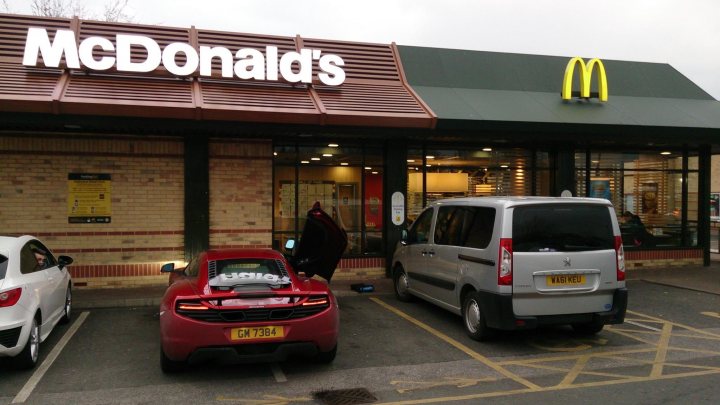 A car parked in front of a building - Pistonheads - The image captures a scene at a Mcdonald's restaurant in a parking lot. The McDonald's sign is prominently displayed above the main entrance. There are a few vehicles parked in the lot, including cars and a van that appears to be a minivan. A car is particularly noticeable, having removed its rear windshield. This creates a scene that seems to be captured on a cloudy day.