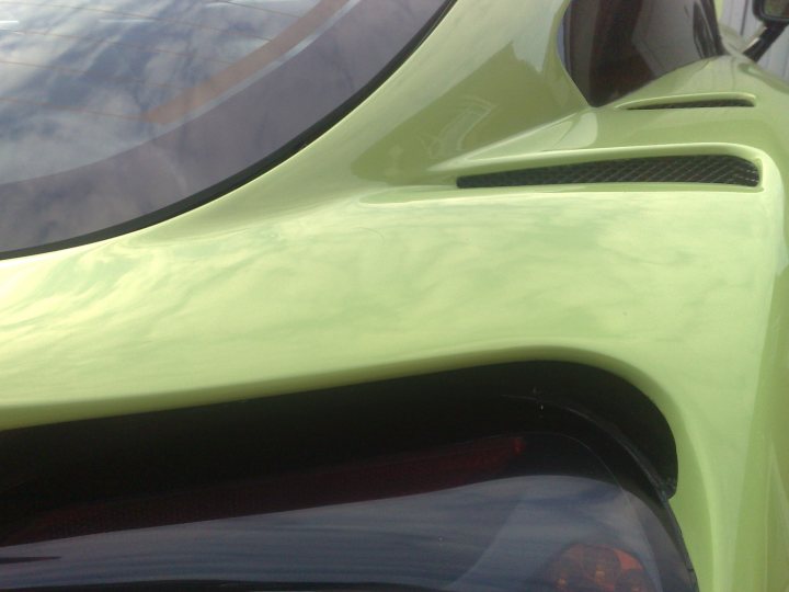 Pistonheads - The image is a close-up photograph of a car's rear taillight area. The backdrop is a hazy, reflective surface which might be the car's window or a mirrored surface. The luminaire component of the mechanical object has a textured pattern that could be an indicator or license plate light mask. The reflection of a tree branch is visible in the window, suggesting the car might be parked with natural light illuminating the glass.