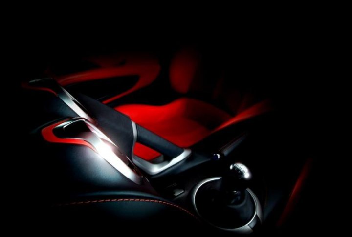 Pistonheads - The image features a close-up view of a sports car steering wheel positioned on the left side of the frame. The wheel, with a black and red color scheme, is adorned with a unique logo and a thumb test is visible. The steering wheel is set against the backdrop of the interior of the car. The wheel is partially illuminated, with a key fob or remote control resting on the bottom of it. The blurred background contrasts with the sharp focus on the steering wheel, emphasizing its design and features.