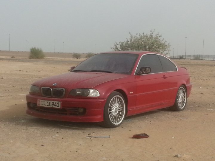 A red car is parked in a field - Pistonheads - The image captures a striking scene on a sandy plane. A BMW car, finished in a bold red hue, commands attention against the muted earthy tones of the desert-like setting. The car's stylish alloy wheels and gleaming headlights reflect the clear skies above. The oxymoron of a luxury vehicle parked amidst the rough terrain adds a unique contrast to the image. Amidst the desolate surroundings, one tree stands out, adding a touch of nature to this otherwise man-made landscape. There's also a single parking meter in the background, a hint of order amidst the open expanse.