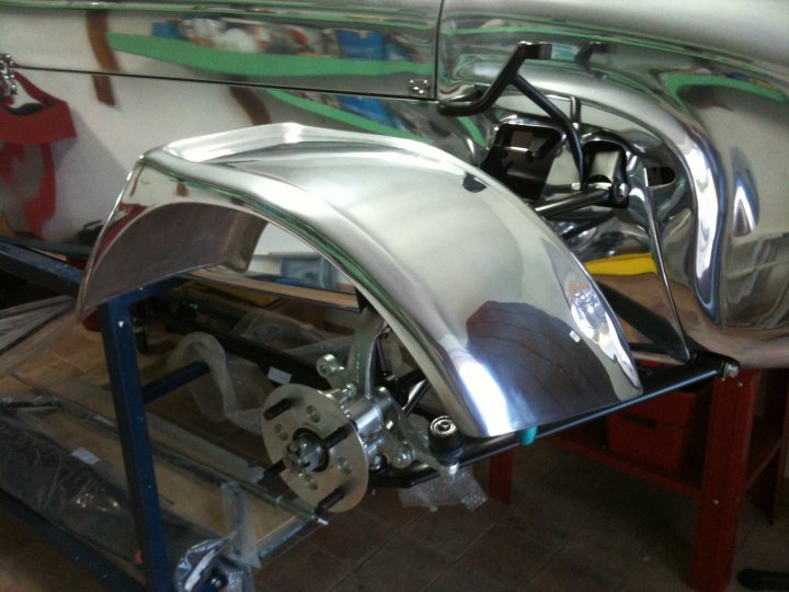 Nuvite Pistonheads - In the image, a front bumper of a silver car is being assembled on a work bench. This process involves fixing several components such as the bumper, front grille, and headlights. The components are easily visible due to the car's shiny silver surface. The backdrop features a white wall and red industrial shelving, indicating an enclosed workshop setting.