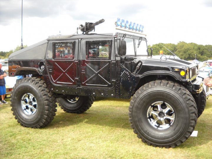 An old truck is parked in a field - Pistonheads - The image features a large, black off-road truck parked on a grassy area. The truck has a prominent chrome bumper and extends high from the ground due to its large tires. The large tires are loosely covered with mud, suggesting recent off-road use or outdoor activities. In the background, there appears to be a person, and the sky is partly cloudy. The overall impression is of a well-equipped off-road vehicle, likely designed for various outdoor endeavors.