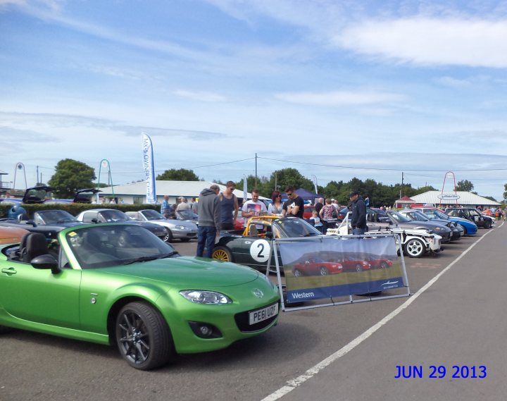 A truck is parked in a parking lot - Pistonheads - The image depicts an outdoor scene at what seems to be a car show or expo, taking place on a sunny day. The primary focus is a vibrant green vehicle, distinguished by a white stripe on its side, parked on the tarmac close to the front of the frame. To the left of this green car, towards the background, there are various other cars and people, suggesting a bustling atmosphere. On the right side of the image, occupying the backdrop, there's a partially visible sign with text and images that seem to be part of the event. Additionally, a timestamp, indicating "JUN 29 2013," is visible at the bottom of the photo.