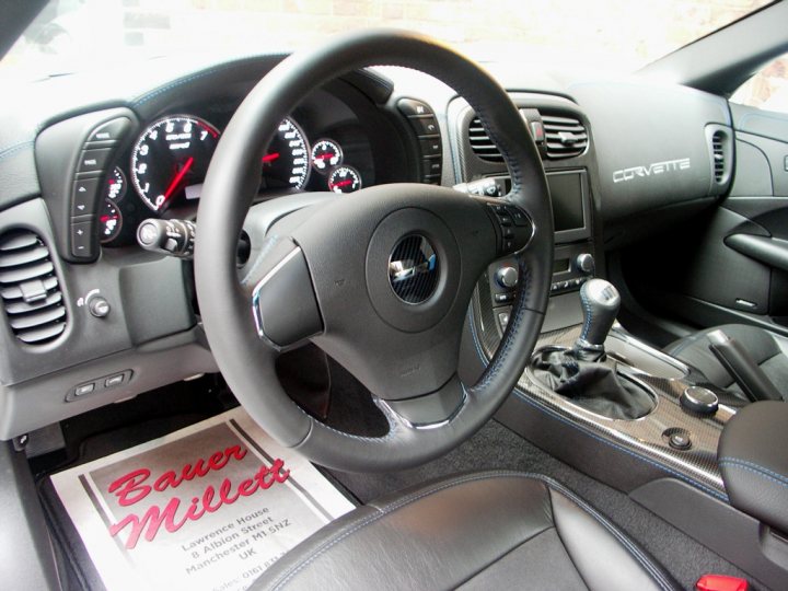 How about some ZR-1 photos to cheer you up? - Page 1 - Corvettes - PistonHeads - The image is taken from the perspective of sitting inside a vehicle looking at the steering wheel. The steering wheel is black with a central metallic control knob. Above the steering wheel, there is a car dashboard showing various instruments and gauges, including a speedometer, an engine temperature gauge, a fuel gauge, and a tachometer. The dashboard also has a digital display screen and air vents on either side. To the left of the steering wheel, there is a black shifter knob, possibly for an automatic transmission, given its position and the visibility of the transmission panel below it. The modern style of the dashboard and the design of the steering wheel suggest that the vehicle has a sleek and contemporary interior. There are no immediate texts or distinctive texts legible in this image.