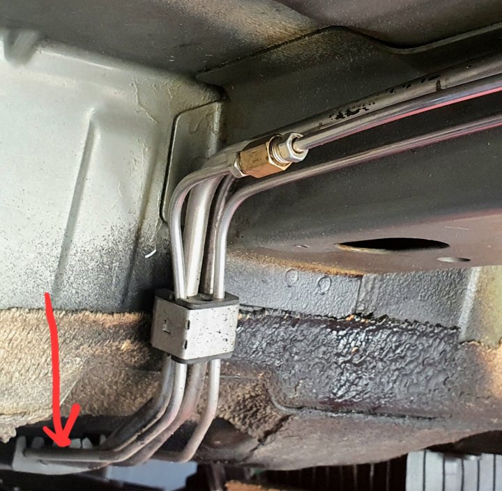 Brake Line Help!! - Page 1 - HSV & Monaro - PistonHeads UK - The image shows a vehicle's underside, focusing on the metal chassis and various wires and cables. There are multiple hoses running along the bottom of the car, with one prominently marked by an arrow pointing to it. This specific hose is connected to a clamp or bracket, suggesting some form of maintenance or repair activity. The vehicle appears to be in the process of being worked on, as evidenced by the exposed chassis and the presence of tools like a wrench. There's also a visible exhaust system running parallel to the hose, indicating that this might be an underbody inspection or repair job.