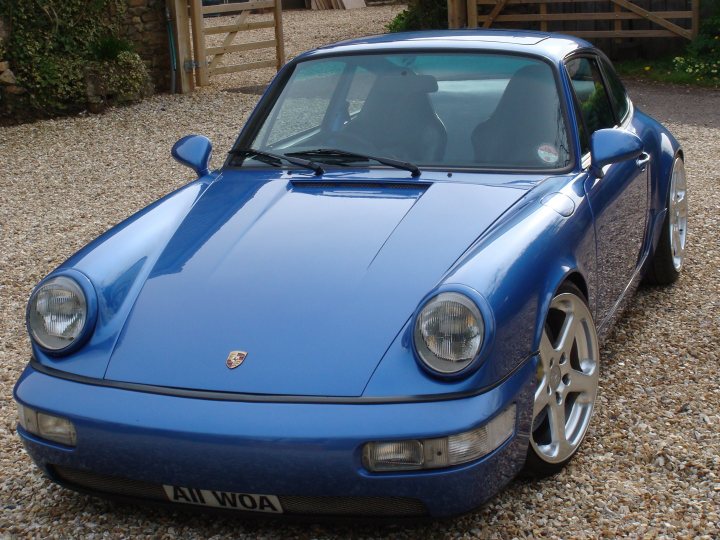 Show us your FRONT END! - Page 43 - Readers' Cars - PistonHeads - The image shows a sleek, blue convertible sports car parked on a gravel driveway. The car is a Porsche, as indicated by the crest and plate number starting with "AIW." Its polished wheels and shiny bodywork suggest it's well-maintained. The car's top is down, revealing a spacious interior and the horizontal louvers over the rear side windows, a signature design element for Porsche's convertibles.