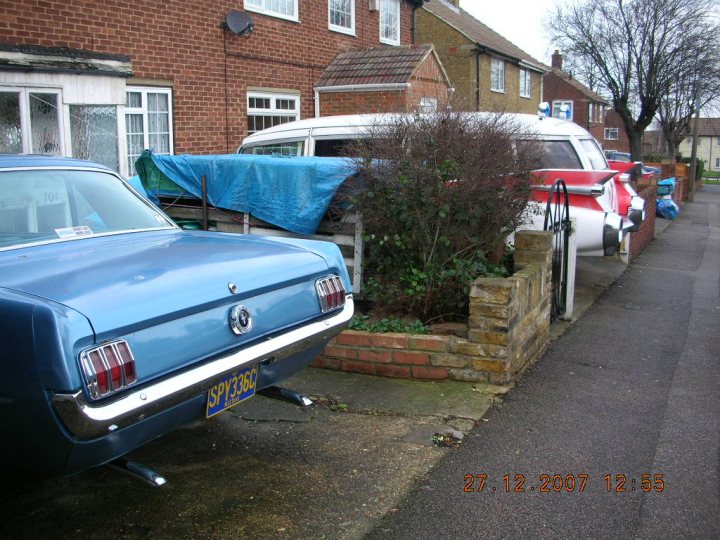 Relics Pistonheads Side Road - The image shows a street scene with a blue classic car parked on the side of the road. Behind the car is a row of parked vehicles, including another classic car and a van, both of which also appear to be parked against a curb on the other side of a fence. To the left of the image is a tree-lined sidewalk with a few vehicles and items on it. The date stamp on the image indicates it is from December 2007.