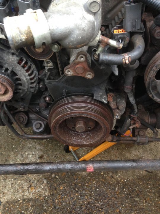 A red and black motorcycle parked in a garage - Pistonheads - The image shows the mechanical underside of an engine. A prominent feature is an engine pulley attached to the shaft. The engine is in a state of disarray with various parts exposed, such as gears, nuts, and belts. There is visible rust and oil indicating a possibly old or poorly maintained engine. The engine is partially covered by a black substance, possibly oil or grease.