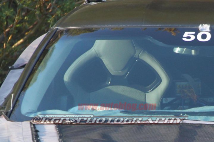 C7  Bucket seats and glimpse of the new steering wheel - Page 1 - Corvettes - PistonHeads - The image is a close-up photograph of the interior of a vehicle focused on the driver's seat. The driver's seat features a colorful and patterned artistic style on the seat cushion, primarily in red with subtle black and white outlines, which is not a common design seen in standard vehicles. The seat is positioned upright, and the person taking the photograph's reflection can be seen in the shiny surface of the metal, indicating that the photograph was likely taken with a watermark of "kstrongphotography.com." There is a visible number "50" on the back of the vehicle's interior, but the context or relevance of this number is not clear from the image alone.