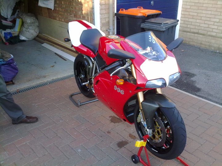 A picture a day....biker banter  - Page 31 - Biker Banter - PistonHeads - The image shows a red and white motorcycle, possibly a Kawasaki, parked on a brick driveway. The motorcycle is leaning on a red and yellow stand, indicating that it is currently not in motion. In the background, there is a garage door and some debris, suggesting that the motorcycle was brought out of its storage unit. There's a person partially visible on the far left of the photo, who seems to be gazing at the motorcycle. The overall setting suggests a residential area.