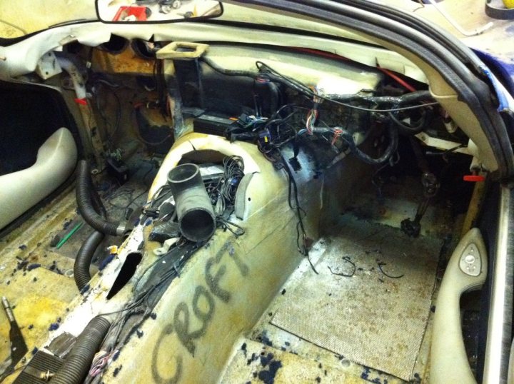 Pistonheads - The photo showcases the interior of a vehicle, focusing primarily on the car's engine area. Scattered across the scene are myriad wires and components, indicative of an ongoing repair or installation process. There's an inscription on the car's floor, but the resolution doesn't allow for clear legibility. The car is in a state of disrepair, with parts missing and the rear trim exposed. This setting suggests meticulous work or a customization project taking place.