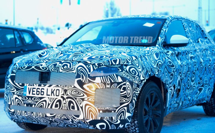 RE: Range Rover Velar teased - Page 19 - General Gassing - PistonHeads - The image shows a car with a unique design on its hood and front fender. The vehicle appears to be a darker color with a wrap around its body . The pattern on the hood resembles abstract circular designs, possibly in shades of white and black. The car is parked in a snowy setting with other vehicles visible in the background. "MOTOR TREND" is printed on the window, suggesting the photo may have been taken by a media outlet specializing in automotive content. The style of the image is a real-life photograph with a focus on the car's detail and vibrant coloration against the contrasting snowy background.