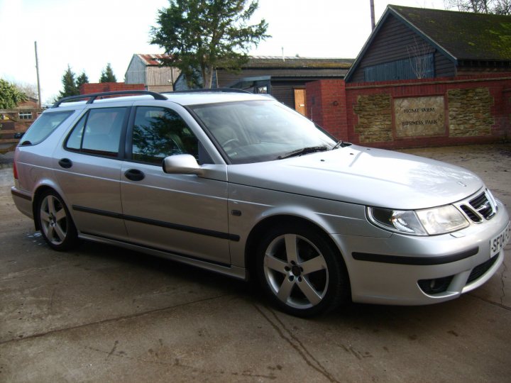 So what car have you been obsessing about today?? (Vol 2) - Page 391 - General Gassing - PistonHeads - The image features a silver SUV parked on a concrete surface. The SUV has a modern design with sleek lines and a tinted rear window. The vehicle is equipped with black rims on the wheels and has a sunroof. In the background, there is a brick wall with a rustic appearance and a wooden door. The sky is visible and appears to be partially cloudy. The overall setting suggests a quiet, possibly residential area.