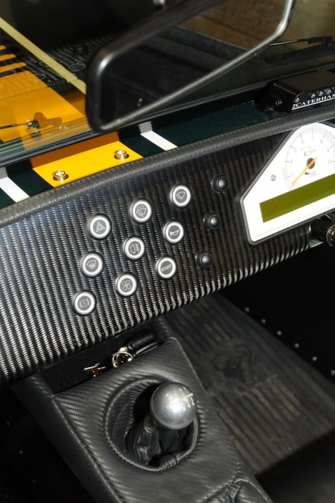 New Style Dash Switches on my R500 - Page 1 - Caterham - PistonHeads - The image depicts a close-up view of a car's interior door panel. This panel is made of a fabric with red stitching. On the right side of the panel, there's a silver door lock. Above the lock, there's a window control button in the form of a bar and below it, a passenger lock button. Additionally, there are indicators with yellow and red lights, which, depending on the context, may represent open and close functions for the window or the passenger lock. The interior of the car appears to be immaculately clean and well maintained.