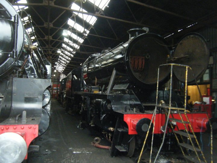 Loco sheds and other railway buildings.... - Page 5 - Boats, Planes & Trains - PistonHeads UK - The image depicts an indoor setting that appears to be a train station or maintenance facility. There are several trains of different sizes and types, including vintage locomotives. The trains are parked closely together on what looks like tracks. The facility has a large open space with high ceilings, and it is well-lit. On the right side of the image, there's an area where parts of the trains are being worked on or maintained. The presence of tools and machinery indicates that this could be a train workshop or depot. There is no text present in the image to provide additional context about the location or the purpose of the facility.