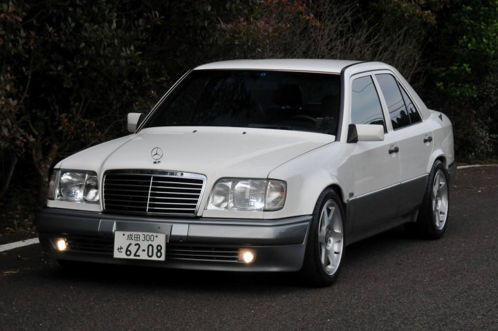 Designs they just got right'? (Rose tinted nostalgia abound) - Page 8 - General Gassing - PistonHeads - In the image, a white Mercedes sedan is parked on a dark asphalt road. The car is positioned at a slight angle to the camera, giving a view of both the front and side of the vehicle. The Mercedes emblem is visible on the grille of the car and it bears a license plate with the text "C6208" over it. The car is the central focus of the image, with a hint of greenery on the left side in the background. The overall scene suggests a quiet, nighttime setting.