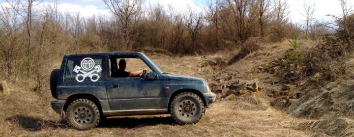 Pistonheads - The image features a blue truck parked on a dirt road surrounded by trees. The vehicle occupies the left side of the frame and is directed towards the right side of the photo. The truck's bed appears to be loaded with objects, but their details are not clear. The weather seems to be overcast, with clouds filling the top portion of the sky. The terrain suggests a rural or remote area, as there is no visible infrastructure or urban development in the vicinity.