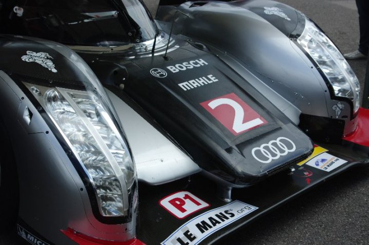 Anyone been to the Moving Motorshow before? - Page 1 - Goodwood Events - PistonHeads - The image captures a corner view of a sleek racing car. It features an Audi, as indicated by the prominently displayed Audi logo on the side and front. The car bears the number 2, and has the text "P1" on the front, suggesting it's designed for racing. Its front spoiler is also visible, adding to the aerodynamic attributes of the car. The dark metallic body of the vehicle contrasts with the red elements, creating a striking visual.