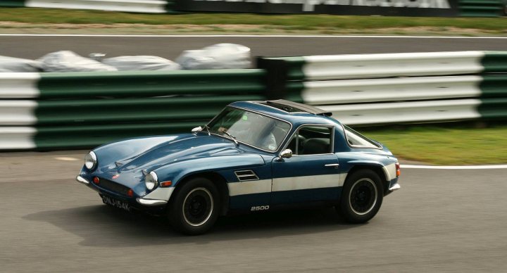 Early TVR Pictures - Page 159 - Classics - PistonHeads - This image captures an exciting moment of a race car in motion on a racing track. The car is a striking blue with a white stripe, resembling the traditional colors of iconic racing teams. The vehicle is leaning into a turn, demonstrating the agility and speed inherent in race car driving. The track itself is clearly marked with a series of green and white barriers that line the courses, a common safety measure in professional racing. The car appears to be in a dynamic racing motion on the track, adding a sense of thrill and competition to the image.