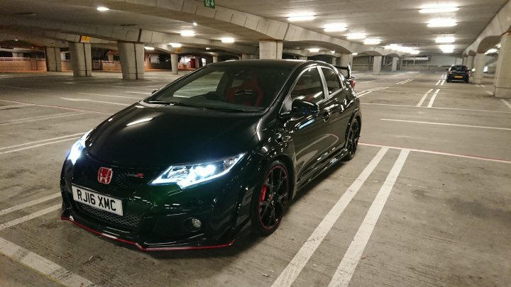 Type R - Page 1 - Readers' Cars - PistonHeads - The image shows a black car parked in a parking lot. It appears to be an Honda Accord, with distinctive customizations including a body kit and red accents. The vehicle is facing the camera, and it has tinted windows. In the background, there's a building with a white facade and several vehicles are visible in the parking lot.