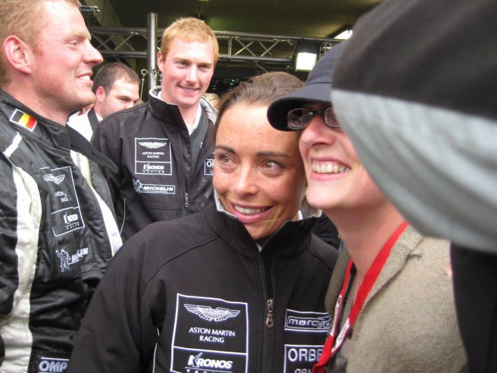 Pistonheads - The image portrays a jovial gathering of people in what appears to be a celebratory or promotional setting. There is a focus on a man and a woman who are hugging and laughing, indicating a sense of joy and camaraderie. The man is wearing glasses and a jacket that reads "MERCEDES," suggesting a connection to the Mercedes racing team. The background is slightly blurred, but the people are wearing similar jackets with the words "ASTON MARTIN RACING" and "KRONOS," which further suggests a racing or motor sports context. Another person in the backdrop is also visible wearing a similar jacket. The atmosphere is warm and convivial, with everyone appearing to be in good spirits.