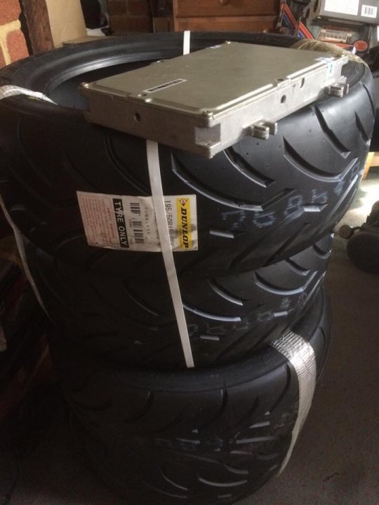 A black suitcase sitting on top of a wooden floor - Pistonheads - In the image, a large set of car tires is piled together on a surface. The tires are black and appear to be in storage or awaiting disposal or recycling. There is a prominent silver metal plate sitting atop one of the tires, adding an interesting contrast to the otherwise monochromatic scene. The tires have a label, possibly indicating crucial information like brand, model, or the last service done, but the small section of it visible in the picture does not provide ample details. The image itself seems to focus on these elements, with the atmospheric background diffused and out of focus.