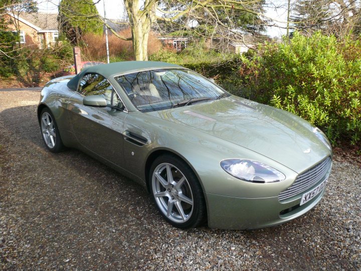 How about an Aston photo thread! - Page 184 - Aston Martin - PistonHeads - The image features a sleek, turquoise Aston Martin car parked on a gravel driveway. The vehicle's design, with its long and aerodynamic form, is evident. The car is positioned diagonally within the frame, showing off the front right wheel and headlight. The background is blurred but suggests a setting with greenery and a residential area. Dropping a pin indicates a neighborhood with houses and a patch of bare ground nearby.