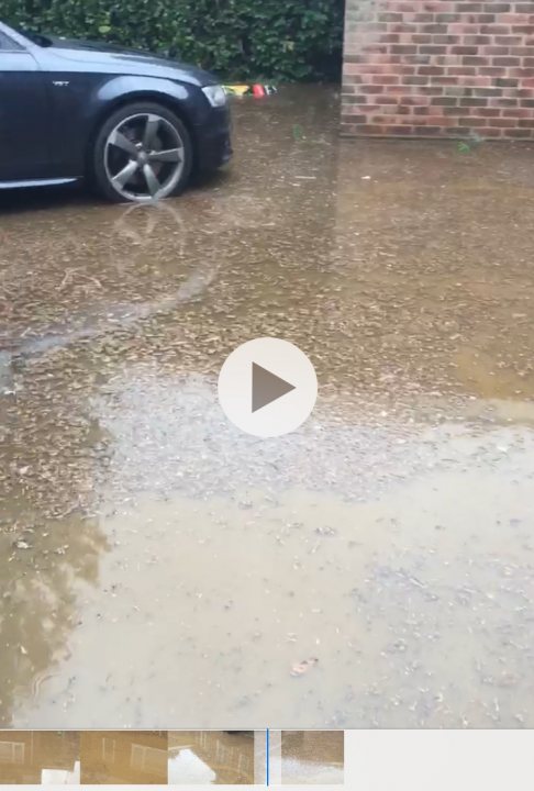 House buying - Seller states No to flooding - Page 1 - Homes, Gardens and DIY - PistonHeads - The image shows a flooded street scene where water has submerged the road, up to the level of the vehicle. A car is partially submerged in the water, with only its roof visible above the flood level. There are no people or animals visible in the frame. In the foreground, there's an overlay from a video camera, showing that someone was recording this event at the time of the image. The street appears to be residential, with houses visible on either side of the road. The overall atmosphere of the image conveys a sense of urgency and damage due to the flooding.