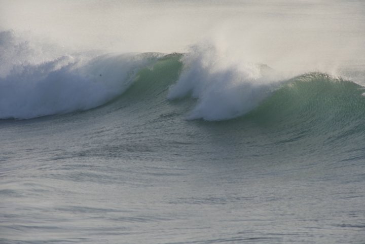 Surfing thread - Page 1 - Sports - PistonHeads - The image captures a stunning ocean scene where a large wave, seemingly alive with movement, dominates the view. The wave is cresting with white foam, indicating its size and power. The ocean water around the wave appears calm, starkly contrasting with the dynamism of the wave itself. The horizon line in the distance suggests a vast expanse of ocean, creating a sense of scale and awe. Overall, the image conveys the raw and unpredictable beauty of the natural world.